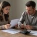 Un couple examine des documents liés à un crédit immobilier et à une assurance autour d’une table, dans une ambiance sobre et réaliste.