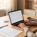 Un homme et une femme consultent un tableau de mensualités de prêt immobilier sur un ordinateur, entourés de documents financiers vierges, d’une calculatrice et de clés de logement.