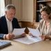 Un couple examine des documents vierges et un graphique abstrait de taux sur un bureau dans une agence bancaire française sobre.