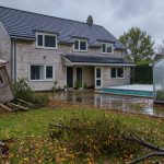 Maison individuelle après une tempête, avec un abri de jardin endommagé, une serre en polycarbonate et une piscine couverte dans le jardin.